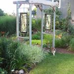 Powder coated metal in gray, with hedge limb across the top and copper weave thru, not seen in photo. Two art glass panels call Whispering Willows on each side of the trellis.  In the midwest we remove the glass panels during the winter months.